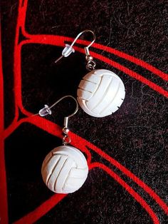 two white round beads are hanging from silver earwires on a black surface with red lines in the background