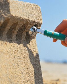 a person holding a green and white toothbrush in their left hand with sand on the ground behind them