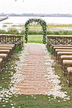 an outdoor ceremony setup with chairs and flowers on the aisle, along with greenery