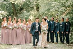 a bride and groom walk with their bridal party in the woods at this wedding