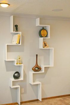 three white shelves with vases and books on them in the corner of a room