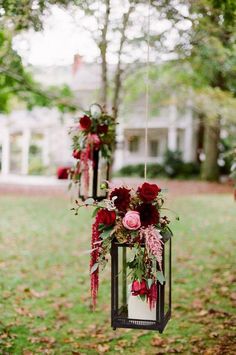 two hanging lanterns with flowers and greenery on them in front of a white house