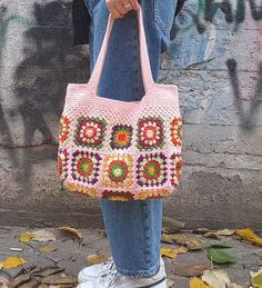 a woman holding a pink crocheted bag in front of a graffiti covered wall