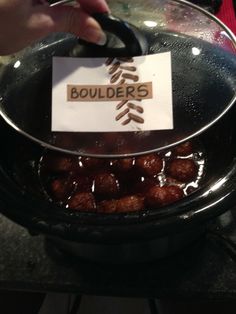 a person holding a sign that says bouilders in front of a pan filled with meatballs