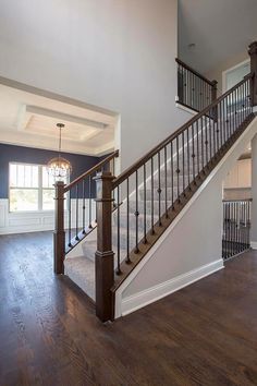 an empty living room with wood floors and white walls is pictured in this image, there are two chandeliers on either side of the staircase