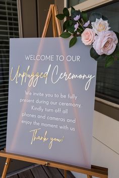 a welcome sign with pink flowers on it and a wooden easer in front of a window