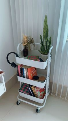 a three tiered shelf with books and plants on it in front of a window