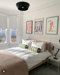 a bed sitting in a bedroom next to two windows with pictures on the wall above it