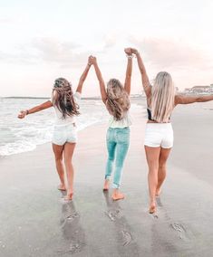 three girls are standing on the beach with their arms in the air