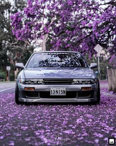 the car is parked on the side of the road with purple flowers all over it