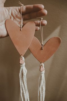 two wooden hearts hanging from strings in the palm of someone's hand, on a beige background