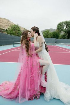 two women in wedding dresses kissing on a tennis court