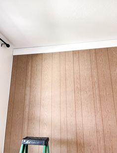 a green step stool sitting in front of a wooden wall with wood paneling on it