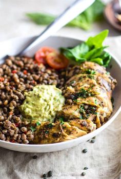 a white bowl filled with meat, beans and guacamole on top of a table