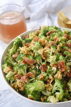 a white bowl filled with broccoli and nuts next to a glass of wine