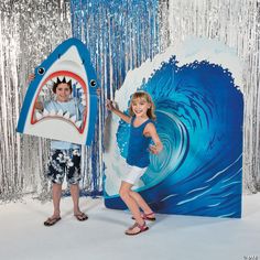 two children posing in front of a backdrop with a shark and a girl holding an umbrella