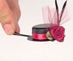 a person is holding a small hat with a rose on the top and a ribbon attached to it