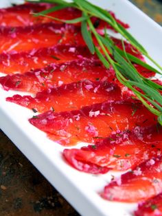 some red food on a white plate with green garnish and sprigs