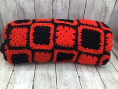 an orange and black crocheted pillow sitting on top of a wooden floor