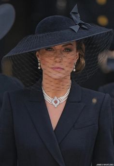 a woman wearing a black hat and jacket with pearls on the collar, standing in front of other people