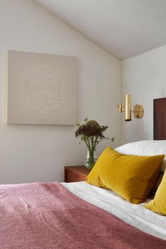 a bed with yellow and red pillows in a bedroom next to a painting on the wall