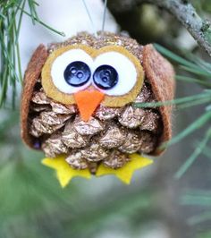 an owl ornament hanging from a pine cone on a tree branch with blue eyes