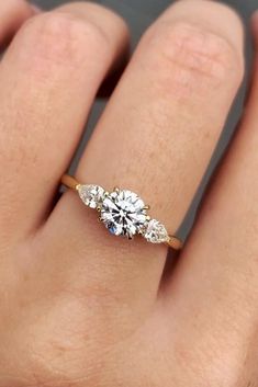 a woman's hand with a three stone ring on her left and an engagement ring on the right