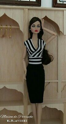 a doll is posed in front of a wooden wall with shelving behind her, wearing a black and white dress