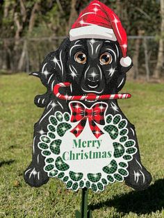 a black dog wearing a santa hat and holding a candy cane in its mouth with the words merry christmas written on it