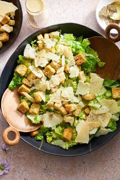 a salad with croutons and parmesan cheese in a black bowl on a table