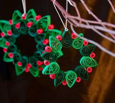 two green and red ornaments hanging from a string on a tree branch, one is shaped like a wreath