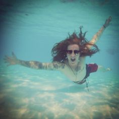 a woman swimming in the ocean with her hair flying through the air and wearing sunglasses