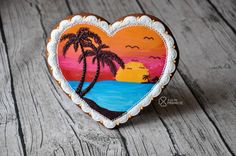 a painted heart shaped cookie with palm trees on the beach and sunset in the background