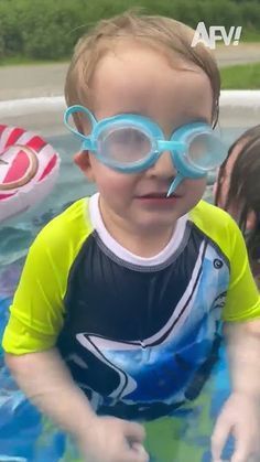 a young boy wearing goggles and swimming in an inflatable pool with his mother