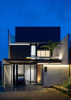 a car is parked in front of a modern house at night with its lights on