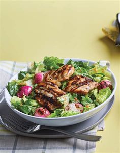 a salad with chicken, radishes and lettuce in a white bowl