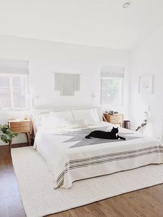 a cat laying on top of a white bed in a room with hardwood flooring