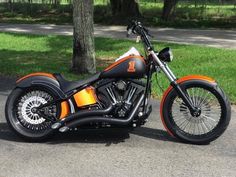 an orange and black motorcycle parked on the side of the road next to a tree