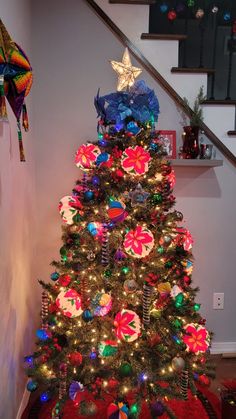 a decorated christmas tree in the corner of a room with stairs and decorations on it