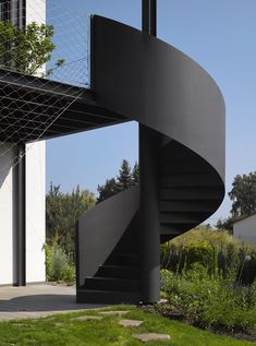 a black spiral staircase in front of a building with grass and bushes on the ground