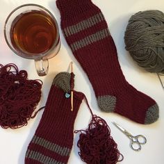 a pair of socks, knitting needles and yarn next to a cup of tea on a table