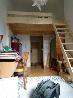 a room with a loft bed, desk and stairs leading to the upper floor area