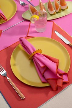 the table is set with pink napkins and yellow plates, silverware and utensils