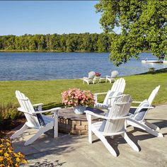 two white adiron chairs sitting on top of a patio next to a lake