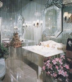 a fancy bathroom with glass walls and chandelier above the bathtub is decorated with pink flowers