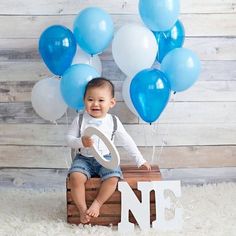 a baby is sitting on a crate with blue and white balloons in the shape of n