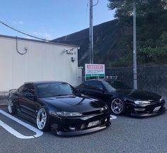 two black cars parked next to each other in a parking lot near a white building