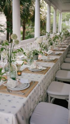 a long table is set with white flowers and place settings for an outdoor dinner party