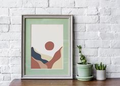 a framed art print sitting on top of a wooden table next to a potted plant