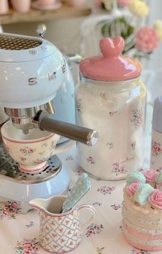 there is a coffee maker and cups on the table next to each other with pink flowers